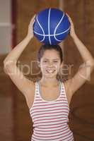 Smiling girl holding basketball on her head in the court