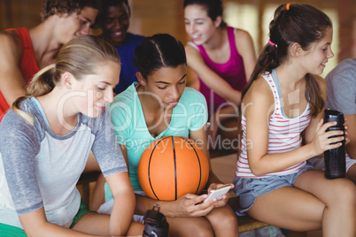 High school kids using mobile phone while relaxing in basketball court