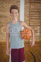 Smiling high school boy holding a basket ball in the court