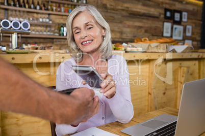 Senior woman making payment through NFC technology on mobile phone