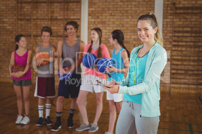 Smiling coach writing on clipboard in the basketball court