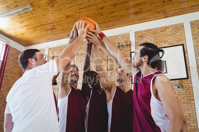 Players and coach holding basketball together in the court