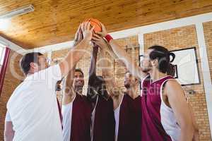 Players and coach holding basketball together in the court