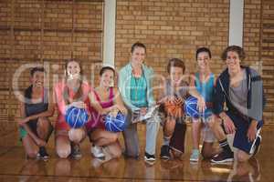 High school kids and coach kneeling with basketball in the court