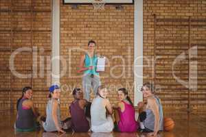 Female coach mentoring high school kids in basketball court