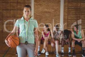 Female coach standing with basketball in basketball court