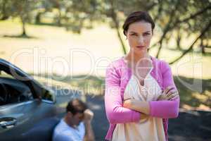 Angry woman standing with man sitting by breakdown car