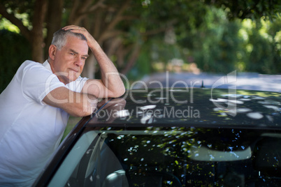 Tensed senior man leaning on car