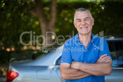 Senior man with arms crossed standing by car