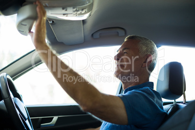 Senior man adjusting rear view mirror in car