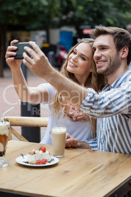 Cheerful couple holding smart phone while sitting at sidewalk cafe