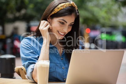 Smiling woman using laptop while sitting at sidewalk cafe