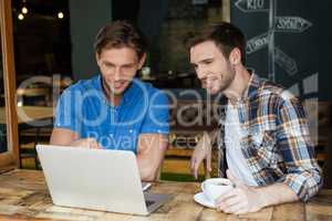 Smiling friends using laptop while sitting at table