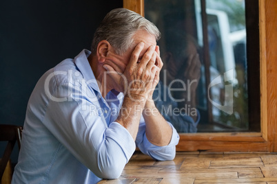 Senior man covering face while sitting at table