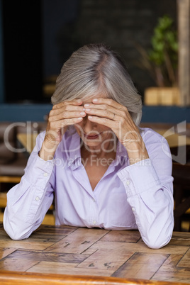Thoughtful senior woman looking down while sitting at table