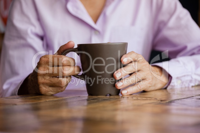 Midsection of woman holding mug while sitting at table