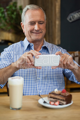 Senior man photographing desert in plate at table