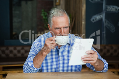 Senior man using digital tablet while drinking coffee