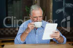 Senior man using digital tablet while drinking coffee