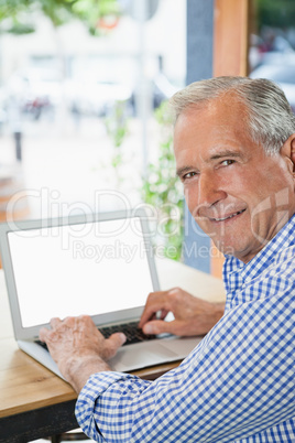 Happy senior man using digital laptop while sitting at cafe shop