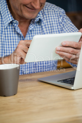 Midsection of senior man using digital tablet while sitting at table