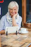 Smiling senior woman using digital tablet while sitting at table