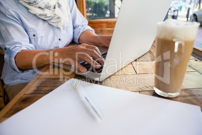 Close up of woman working on laptop computer by cold coffee at table