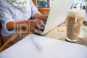 Close up of woman working on laptop computer by cold coffee at table