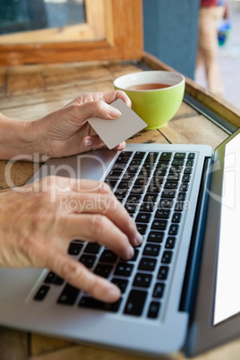 Close of woman typing on laptop while holding credit card at table