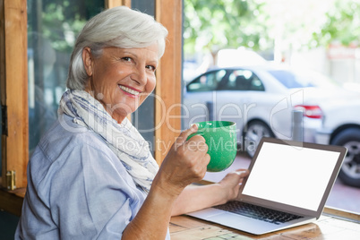 Portrait of smiling senior woman holding coffee cup while sitting at table