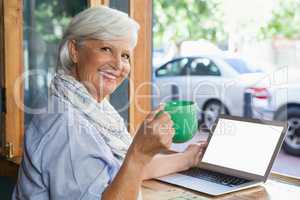 Portrait of smiling senior woman holding coffee cup while sitting at table