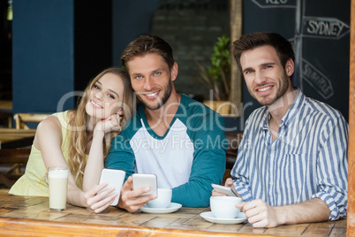 Portrait of smiling friend holding smart phone while sitting by table