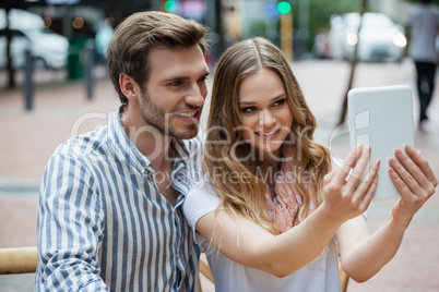 Happy couple holding digital tablet while sitting at sidewalk cafe