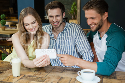 Cheerful friends using mobile phone while sitting by table