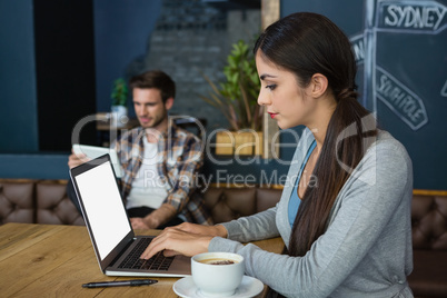 Young woman using laptop while having coffee