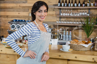 Portrait of waitress standing with hand on hip at counter