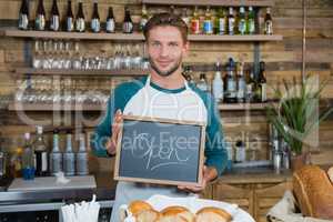 Portrait of smiling waiter holding chalkboard with open sign