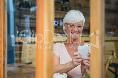 Senior woman using mobile phone while having coffee