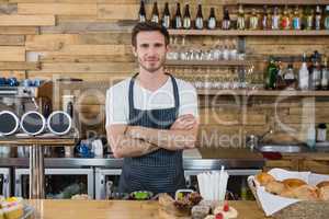Portrait of smiling waiter standing with arms crossed at counter