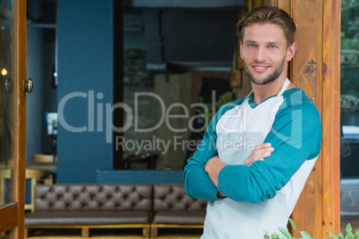 Portrait of smiling waiter standing with arms crossed