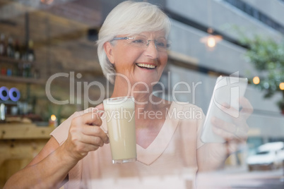 Happy senior woman using mobile phone while having cold coffee