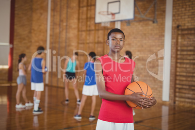 High school boy holding a basketball while team playing in background