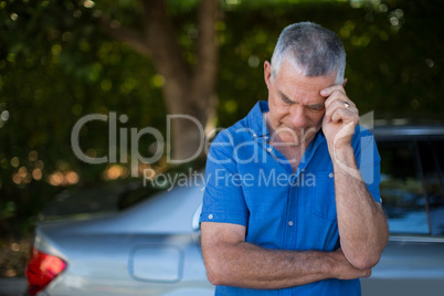 Tensed senior man standing by car