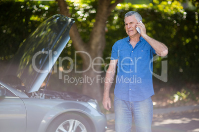 Senior man talking on phone by breakdown car