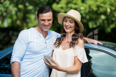 Young woman holding mobile with man by car