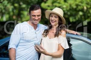Young woman holding mobile with man by car