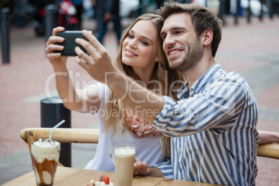 Couple holding smart phone while sitting at sidewalk cafe