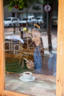 Smiling woman holding mobile phone while sitting at cafe