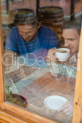 Happy friends using laptop while sitting by window