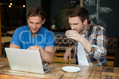 Friends using laptop while sitting at table in restaurant